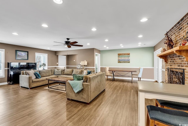 living room featuring light wood-type flooring, a brick fireplace, baseboards, and recessed lighting