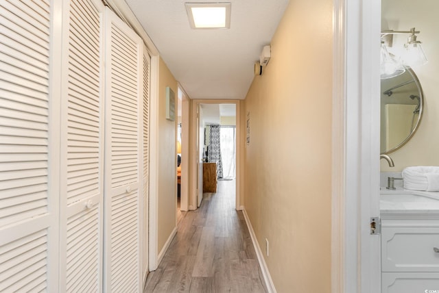 hall with baseboards, light wood-style floors, and a sink