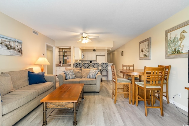 living area with visible vents, baseboards, light wood-style floors, and a ceiling fan