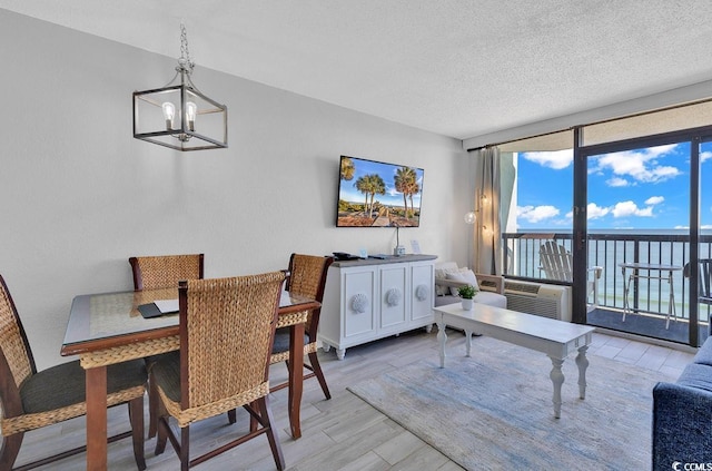 dining space with floor to ceiling windows, a notable chandelier, light wood-style flooring, and a textured ceiling