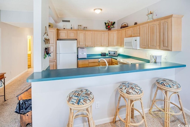 kitchen with white appliances, a kitchen bar, light brown cabinets, and visible vents