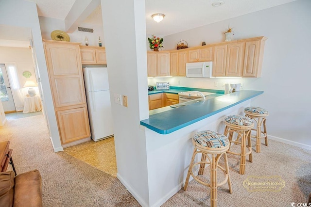 kitchen with light brown cabinetry, white appliances, a breakfast bar, and visible vents