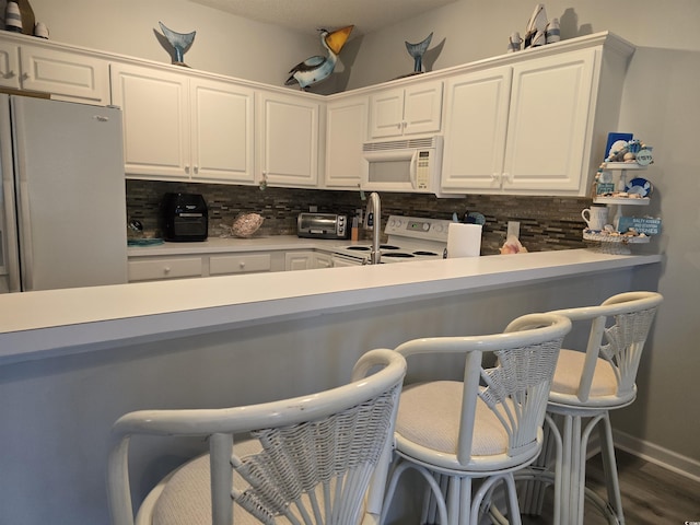 kitchen featuring white appliances, white cabinetry, a kitchen breakfast bar, light countertops, and backsplash