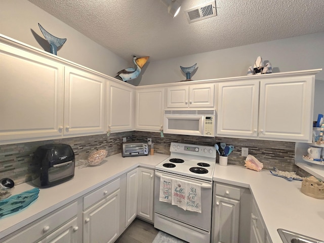 kitchen with tasteful backsplash, light countertops, visible vents, white cabinets, and white appliances