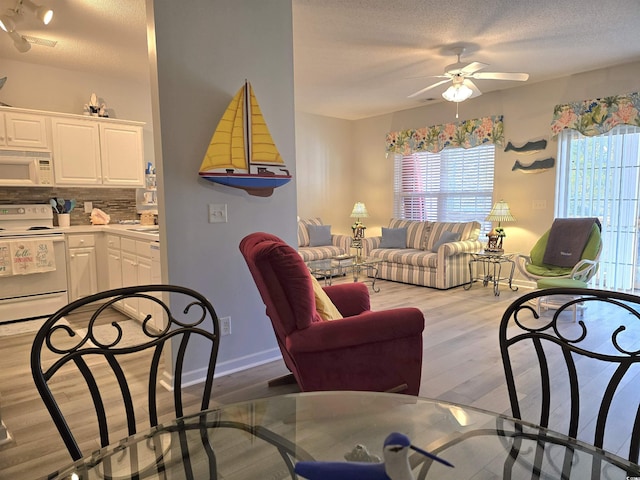 living room featuring a textured ceiling, ceiling fan, visible vents, baseboards, and light wood-style floors