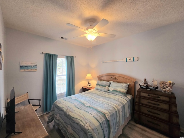 bedroom featuring a ceiling fan, visible vents, a textured ceiling, and wood finished floors