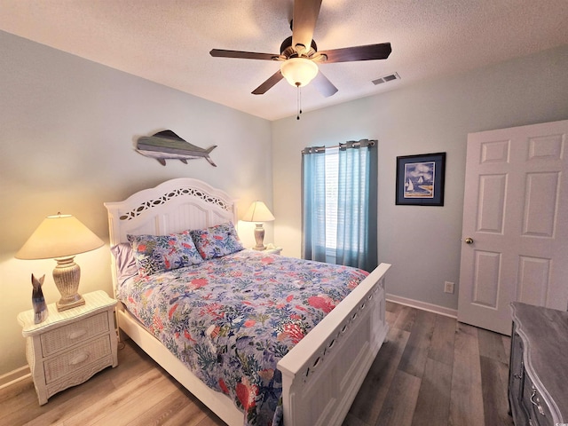 bedroom featuring a textured ceiling, wood finished floors, visible vents, and baseboards