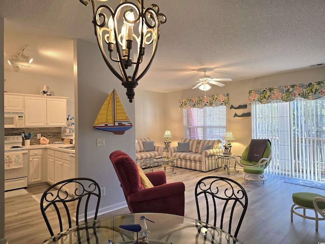 living area featuring visible vents, light wood-style floors, a textured ceiling, baseboards, and ceiling fan with notable chandelier