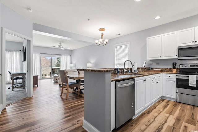 kitchen with light wood-style flooring, a peninsula, white cabinets, appliances with stainless steel finishes, and a sink