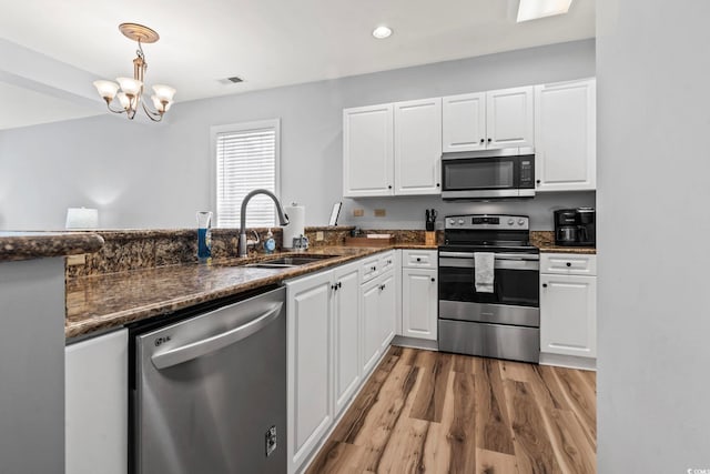 kitchen featuring visible vents, white cabinets, a sink, light wood finished floors, and stainless steel appliances