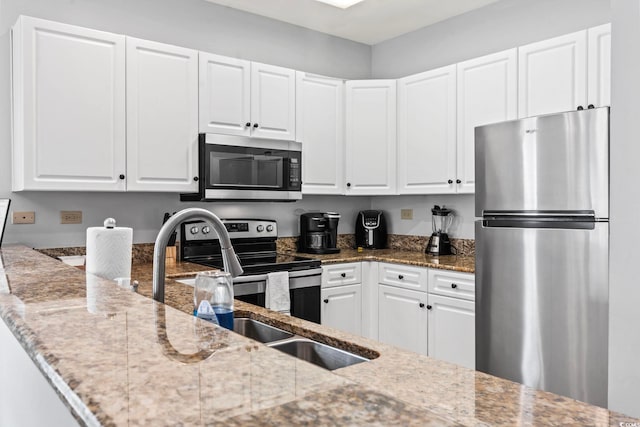 kitchen with stainless steel appliances, light stone countertops, white cabinets, and a sink
