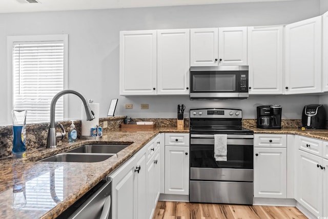 kitchen with a sink, light wood-type flooring, white cabinets, and appliances with stainless steel finishes