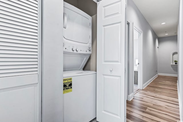 clothes washing area with baseboards, light wood-type flooring, stacked washer / dryer, laundry area, and recessed lighting