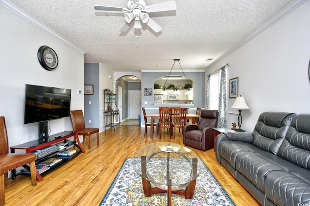 living area with arched walkways, crown molding, light wood-style floors, a ceiling fan, and a textured ceiling