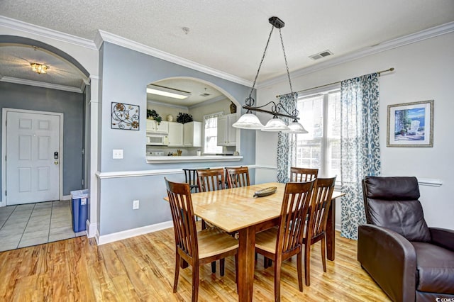 dining area featuring arched walkways, a textured ceiling, visible vents, light wood finished floors, and crown molding