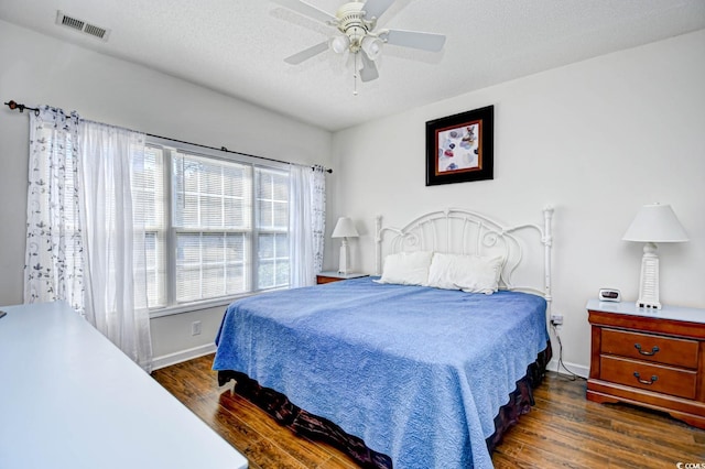 bedroom featuring ceiling fan, a textured ceiling, visible vents, and dark wood-style flooring