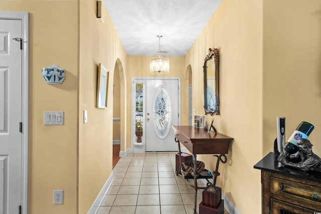 entrance foyer with baseboards, a chandelier, arched walkways, and light tile patterned flooring