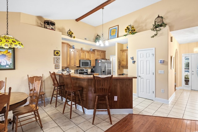 kitchen featuring lofted ceiling with beams, stainless steel appliances, a breakfast bar, a peninsula, and hanging light fixtures