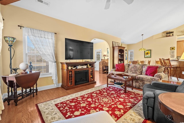 living area with arched walkways, a fireplace, visible vents, vaulted ceiling, and wood finished floors