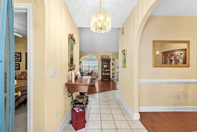 foyer with tile patterned flooring, arched walkways, a chandelier, and baseboards