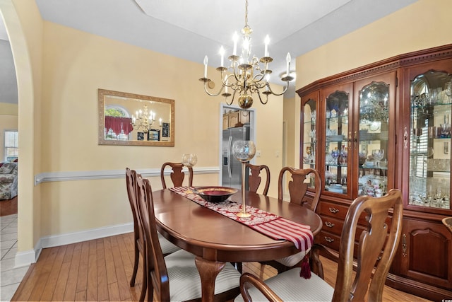 dining space featuring arched walkways, light wood-style flooring, baseboards, and an inviting chandelier