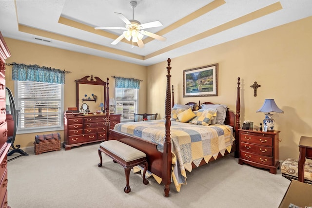 bedroom featuring ceiling fan, light colored carpet, visible vents, baseboards, and a raised ceiling