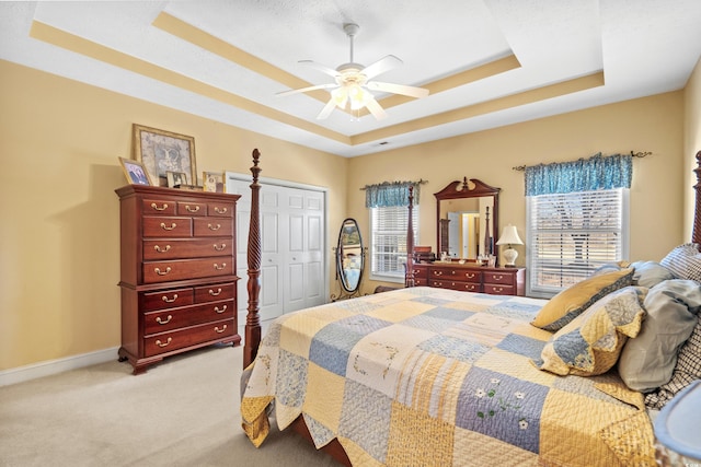 bedroom with baseboards, a ceiling fan, light colored carpet, a tray ceiling, and a closet