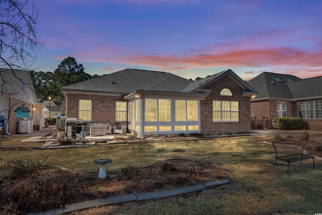 back of property with a yard, a patio, brick siding, and a shingled roof