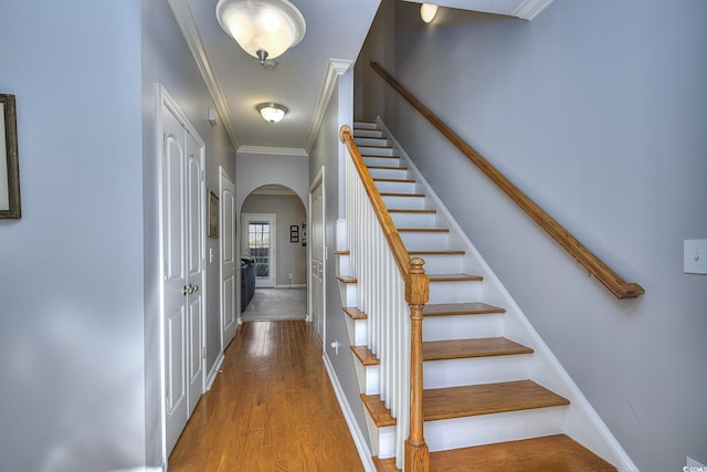 stairs featuring ornamental molding, arched walkways, baseboards, and wood finished floors