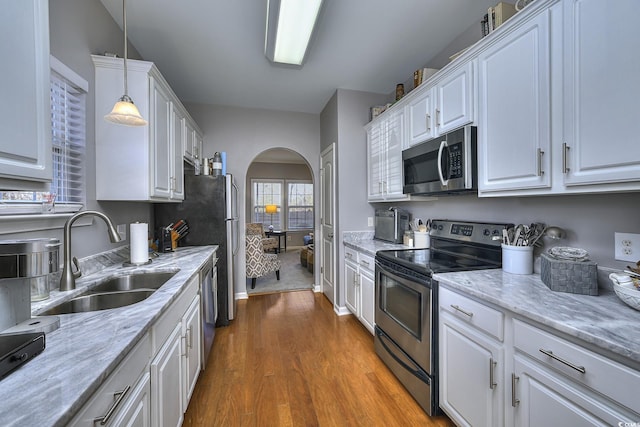 kitchen featuring arched walkways, dark wood finished floors, stainless steel appliances, white cabinetry, and a sink