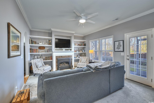 living room featuring carpet floors, a ceiling fan, visible vents, a glass covered fireplace, and crown molding