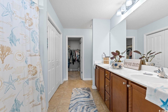 bathroom with double vanity, a sink, a textured ceiling, tile patterned flooring, and baseboards