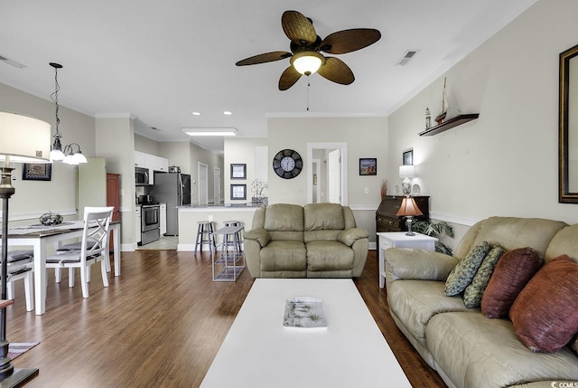 living area featuring visible vents, ornamental molding, dark wood finished floors, and ceiling fan with notable chandelier