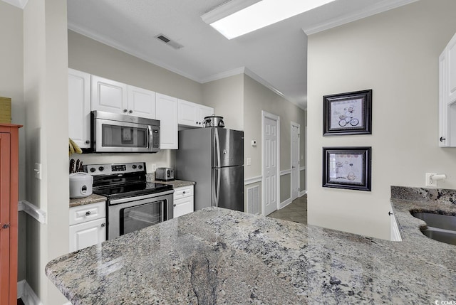kitchen with white cabinets, appliances with stainless steel finishes, ornamental molding, and light stone counters