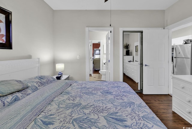 bedroom featuring dark wood-type flooring, freestanding refrigerator, and ensuite bath
