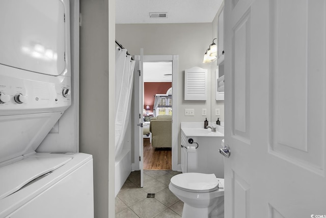 full bathroom with vanity, toilet, tile patterned floors, stacked washer / dryer, and visible vents