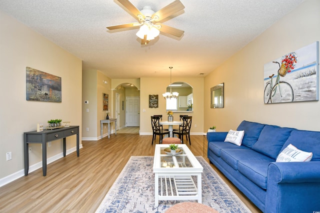 living area featuring arched walkways, ceiling fan with notable chandelier, light wood finished floors, and a textured ceiling
