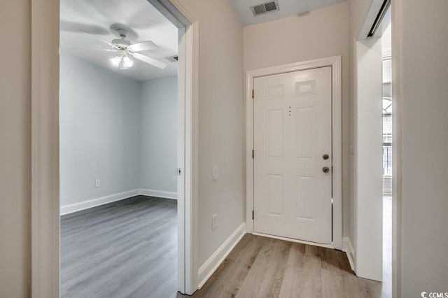 foyer entrance with baseboards, visible vents, ceiling fan, and wood finished floors