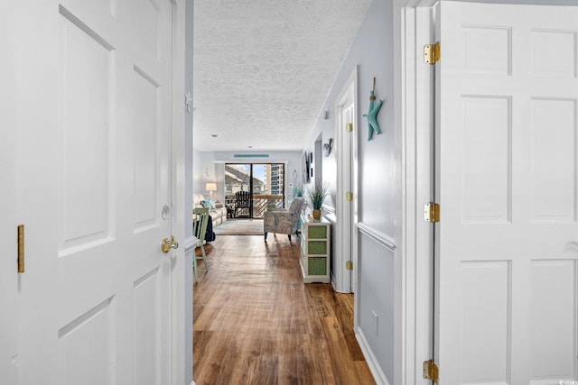 corridor featuring baseboards, a textured ceiling, and wood finished floors