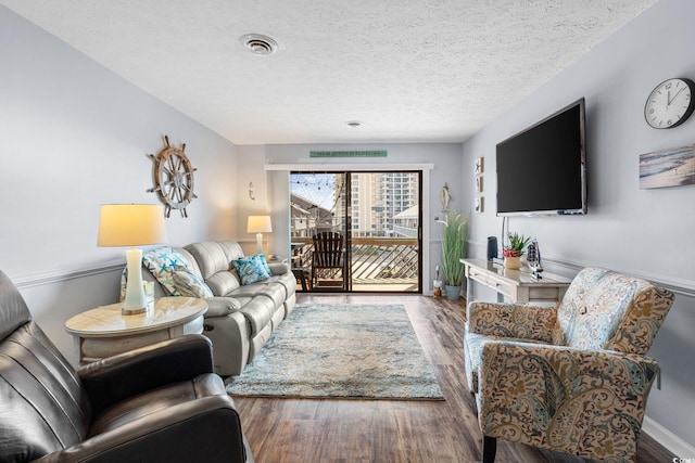 living room with baseboards, a textured ceiling, visible vents, and wood finished floors