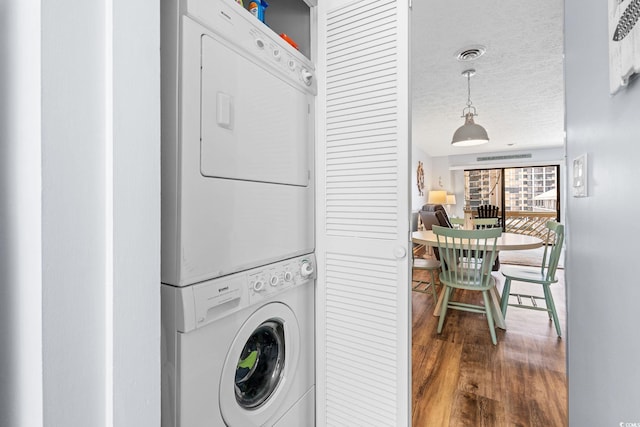 laundry room with stacked washer and dryer, visible vents, a textured ceiling, wood finished floors, and laundry area