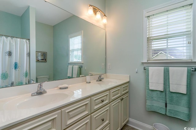 full bath featuring toilet, double vanity, and baseboards