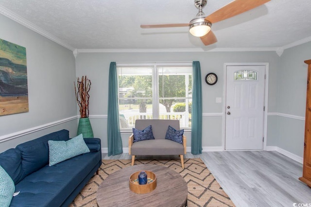 living area featuring light wood-style floors, ornamental molding, ceiling fan, a textured ceiling, and baseboards