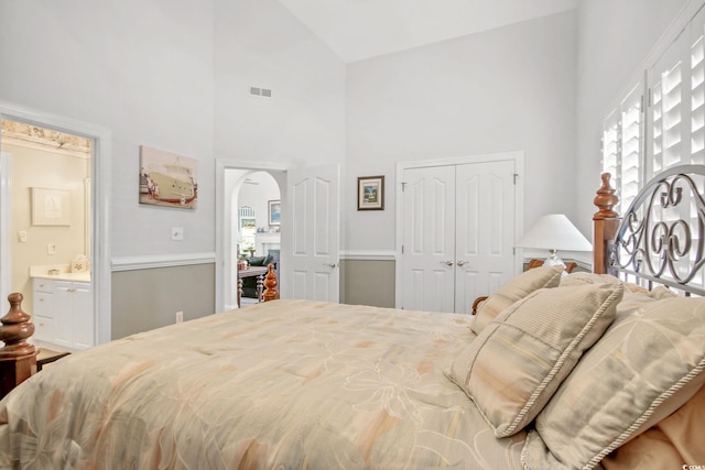 bedroom with visible vents, a closet, ensuite bathroom, arched walkways, and high vaulted ceiling