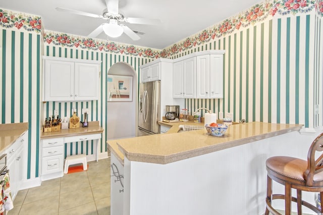 kitchen with wallpapered walls, a sink, light countertops, stainless steel refrigerator with ice dispenser, and a kitchen bar