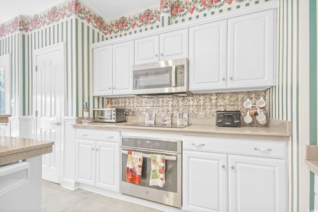 kitchen with stainless steel appliances, white cabinetry, light countertops, and wallpapered walls