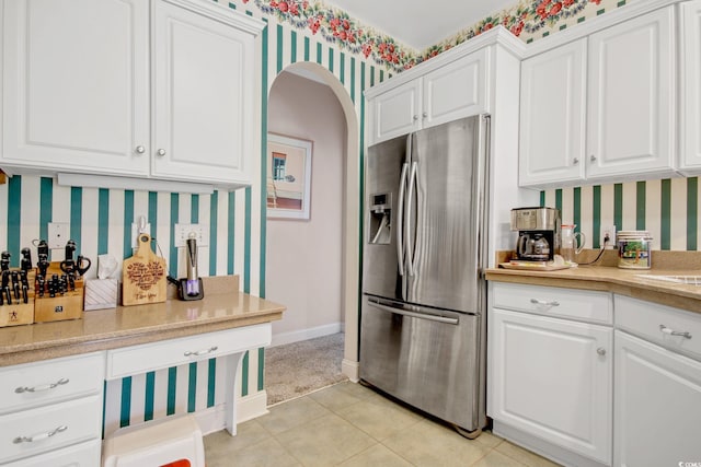 kitchen featuring wallpapered walls, white cabinets, arched walkways, and stainless steel fridge