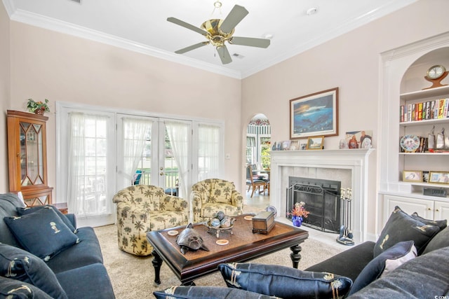 carpeted living room featuring crown molding, built in features, a tile fireplace, french doors, and a ceiling fan