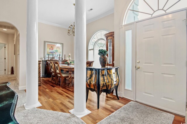 entryway with decorative columns, arched walkways, ornamental molding, and light wood finished floors