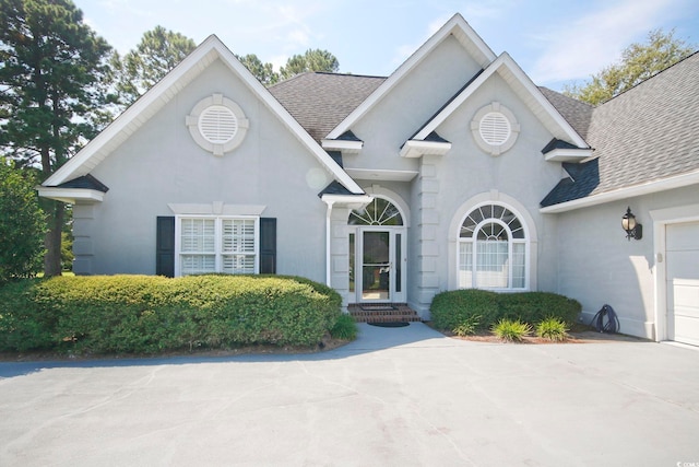 view of front of house with stucco siding, an attached garage, and a shingled roof